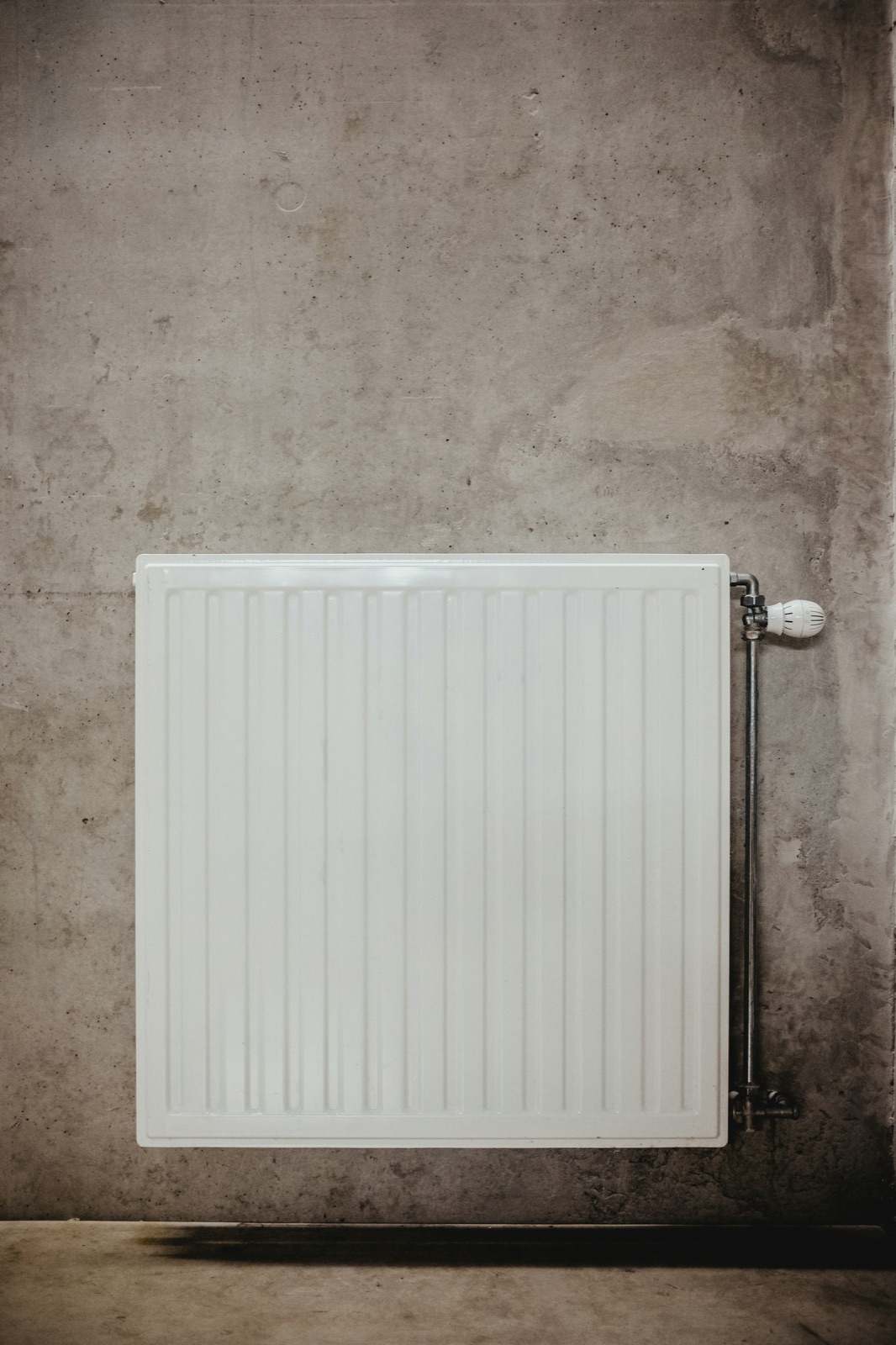 Vit vattenburen panelradiator med termostat mot en grå vägg.